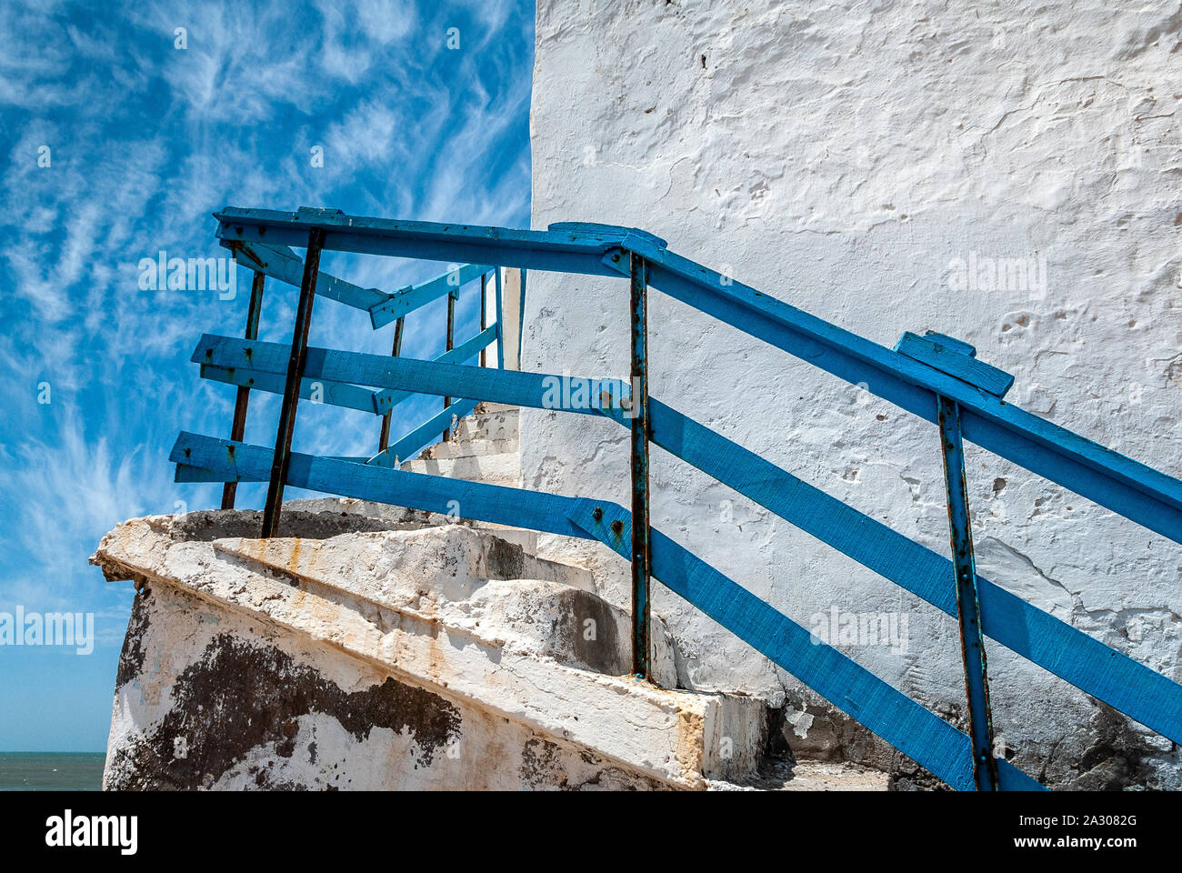 La ringhiera di blu di una scalinata esterna che su un edificio bianco vicino al mare e con un cielo punteggiato di nuvole Foto Stock