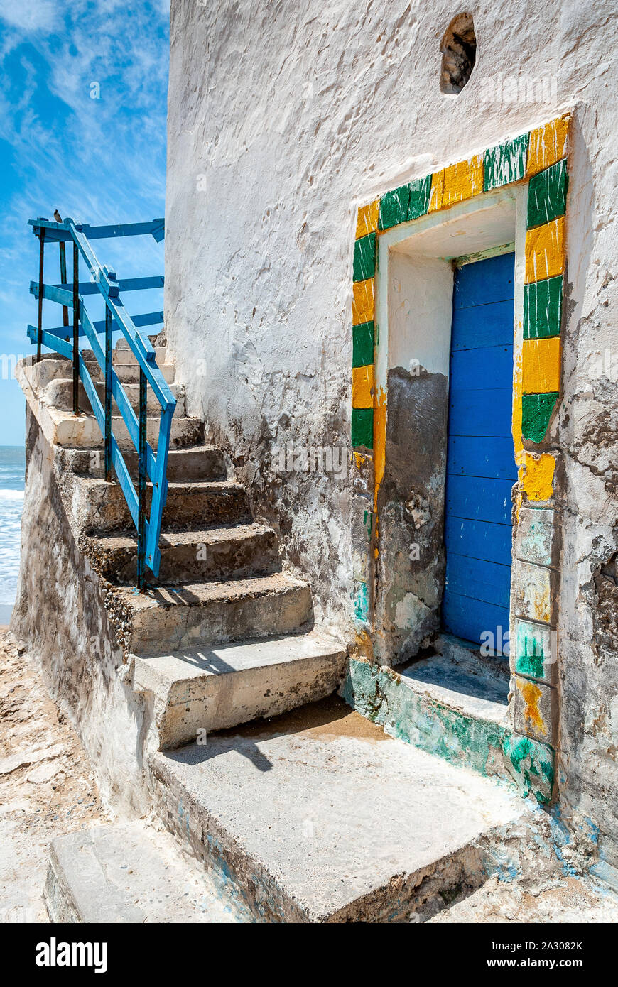 Il giallo e il verde il telaio di una porta blu ai piedi di una scala esterna su un decrepito edificio bianco in Sidi Kaouki, Marocco Foto Stock