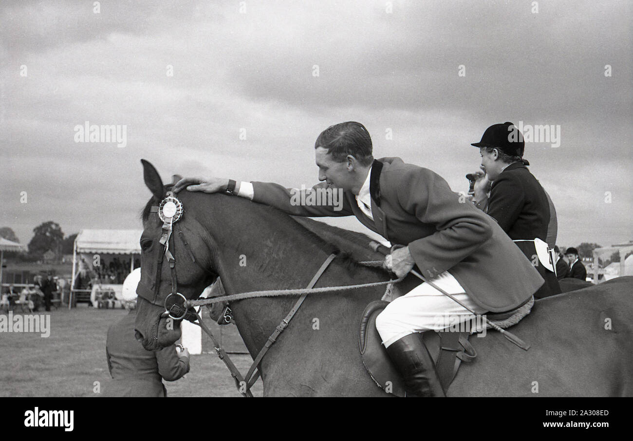 Degli anni Cinquanta, storico, county mostrano fuori dopo un evento showjumping, un maschio di corse del pilota la testa del suo cavallo vincente che ha una coccarda attaccato, Inghilterra, Regno Unito. Foto Stock