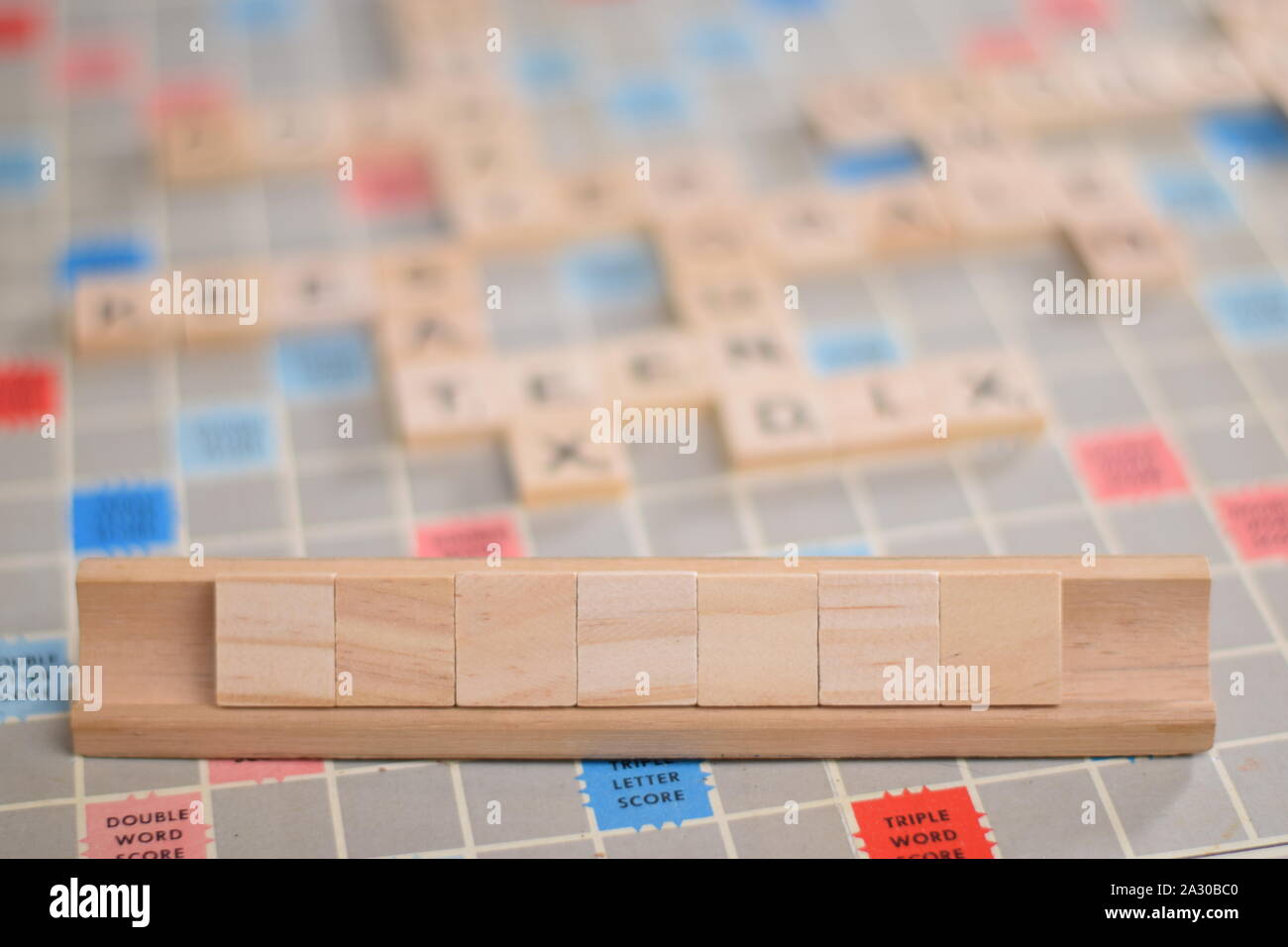 7 vuoto in legno piastrelle scrabble su una piastrella-rack, per voi per riempire la propria parola. Sullo sfondo di una scheda vintage, fuori fuoco con spazio di copia Foto Stock