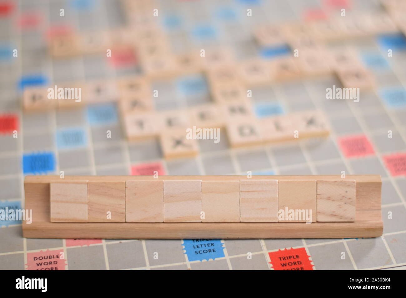8 vuoto in legno piastrelle scrabble su una piastrella-rack, per voi per riempire la propria parola. Sullo sfondo di una scheda vintage, fuori fuoco con spazio di copia Foto Stock
