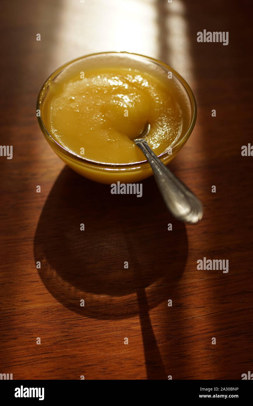 Round ciotola di vetro con il miele e il cucchiaio su una soleggiata tavolo in legno Foto Stock