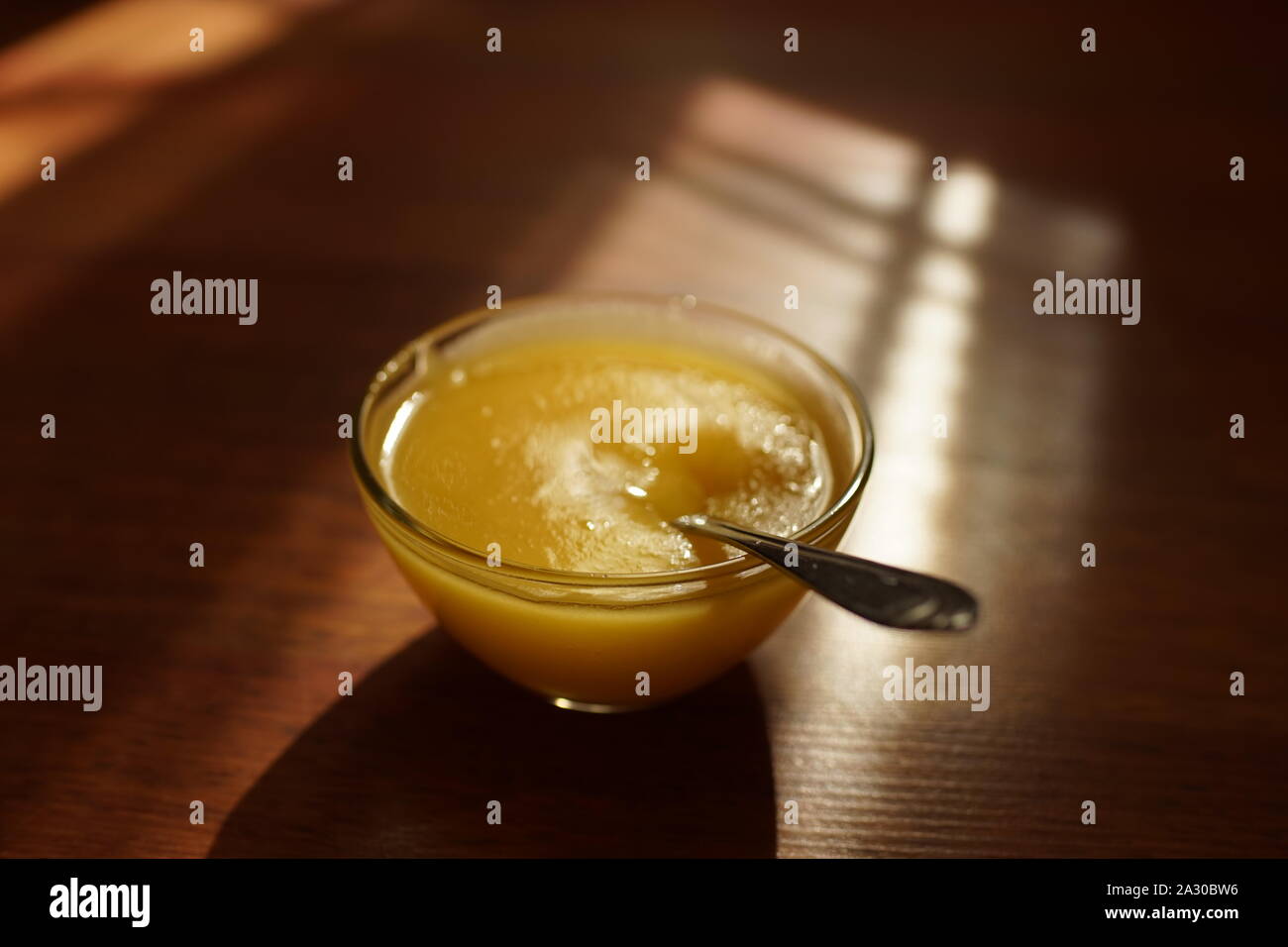 Round ciotola di vetro con il miele e il cucchiaio su una soleggiata tavolo in legno Foto Stock