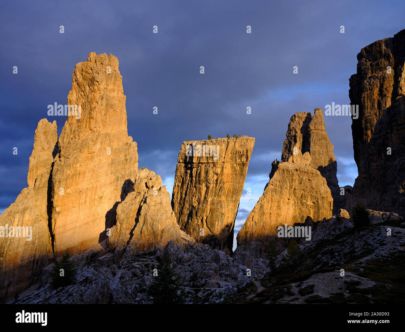Formazioni rocciose grigio chiaro delle cinque Torri che si illuminano di rosso su uno sfondo di nuvole scure al tramonto. Cortina d'Ampezzo, Dolomiti, Veneto, Italia. Foto Stock