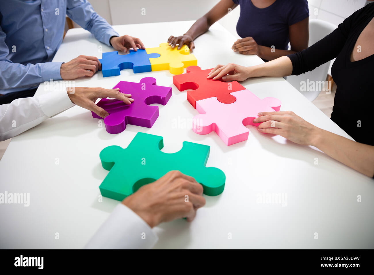 Mani di imprenditori edificio colorato seghetto alternativo puzzle insieme sulla scrivania bianca al lavoro Foto Stock