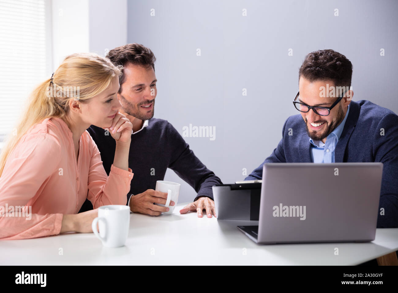 Felice Coppia Giovane consultazione amichevole maschio Advisor finanziario con tazze da caffè alla scrivania in ufficio Foto Stock