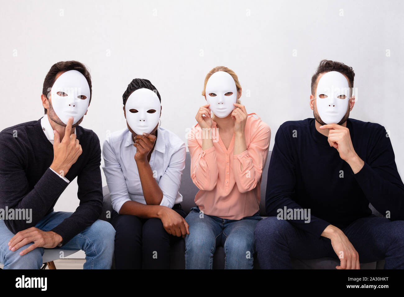 Un gruppo di persone in piedi insieme che copre il volto con maschere bianche Foto Stock