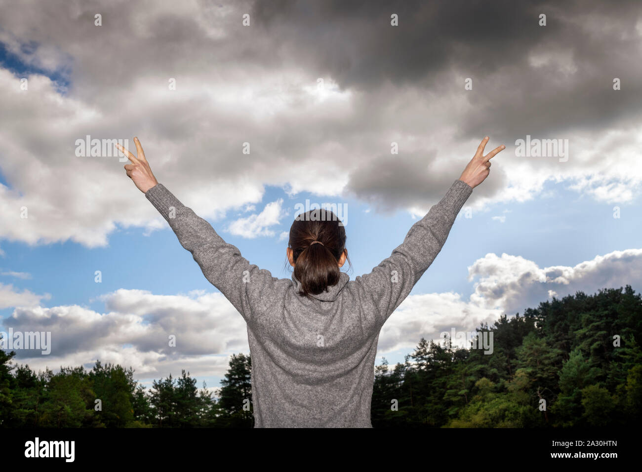 Vista posteriore di una donna con le braccia sollevate a un tempestoso moody sky Foto Stock