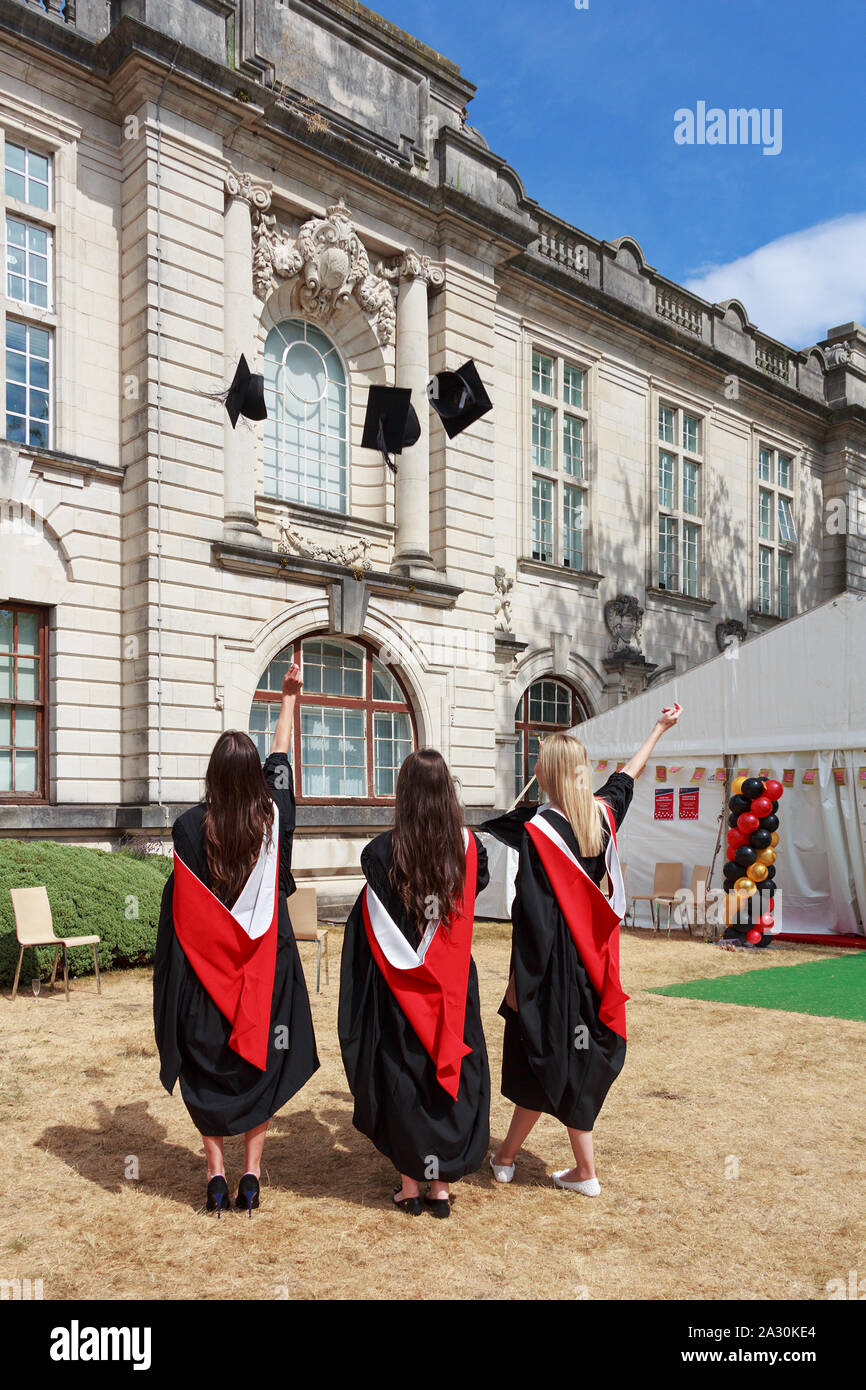 Vista dal lato posteriore di tre ragazze felici di indossare abiti accademico di gettare i tappi accademico nel cortile dell'Università di Cardiff, Cardiff Wales, Regno Unito Foto Stock
