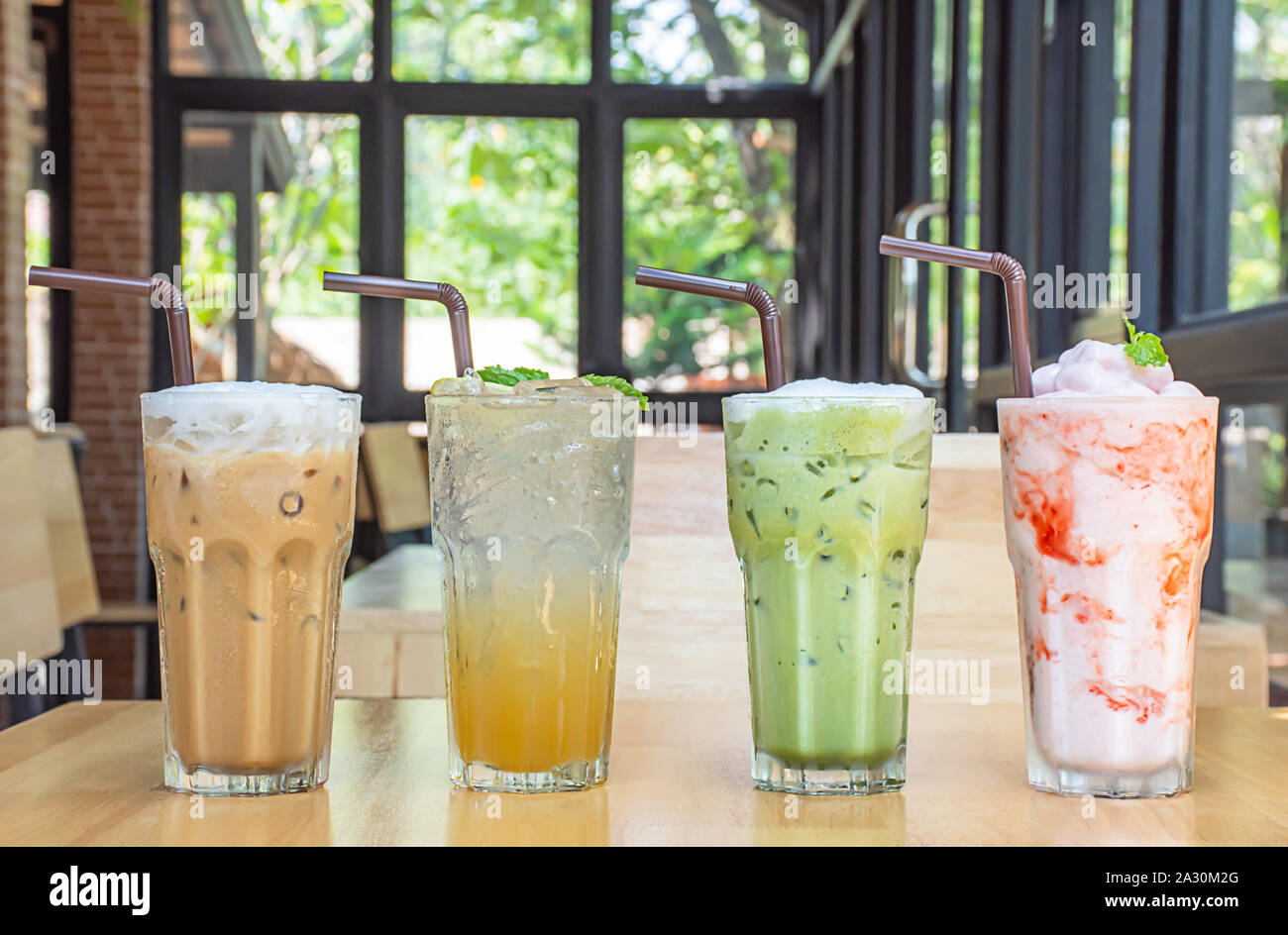 Caffè ghiacciato, miele di Limone , Soda ghiacciata di tè verde e il frullato fragole in vetro sul tavolo di legno sfondo finestre di vetro e l'albero. Foto Stock