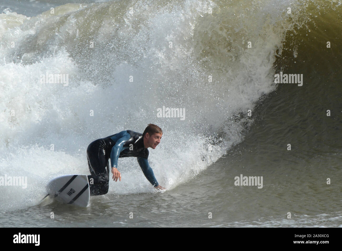 Mano tirati in onda un surfer angoli la sua tavola da surf e il corpo nella sua volta al di fuori del lato inferiore della forma d'onda, temporizzazione il suo turno per impostare la sua cavalcata Foto Stock