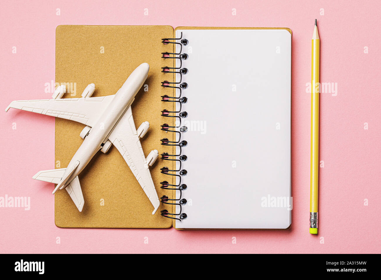 Aeroplano, notebook e matita su un sfondo rosa, vista dall'alto. Concetto sul tema: Come pianificare un volo. Foto Stock