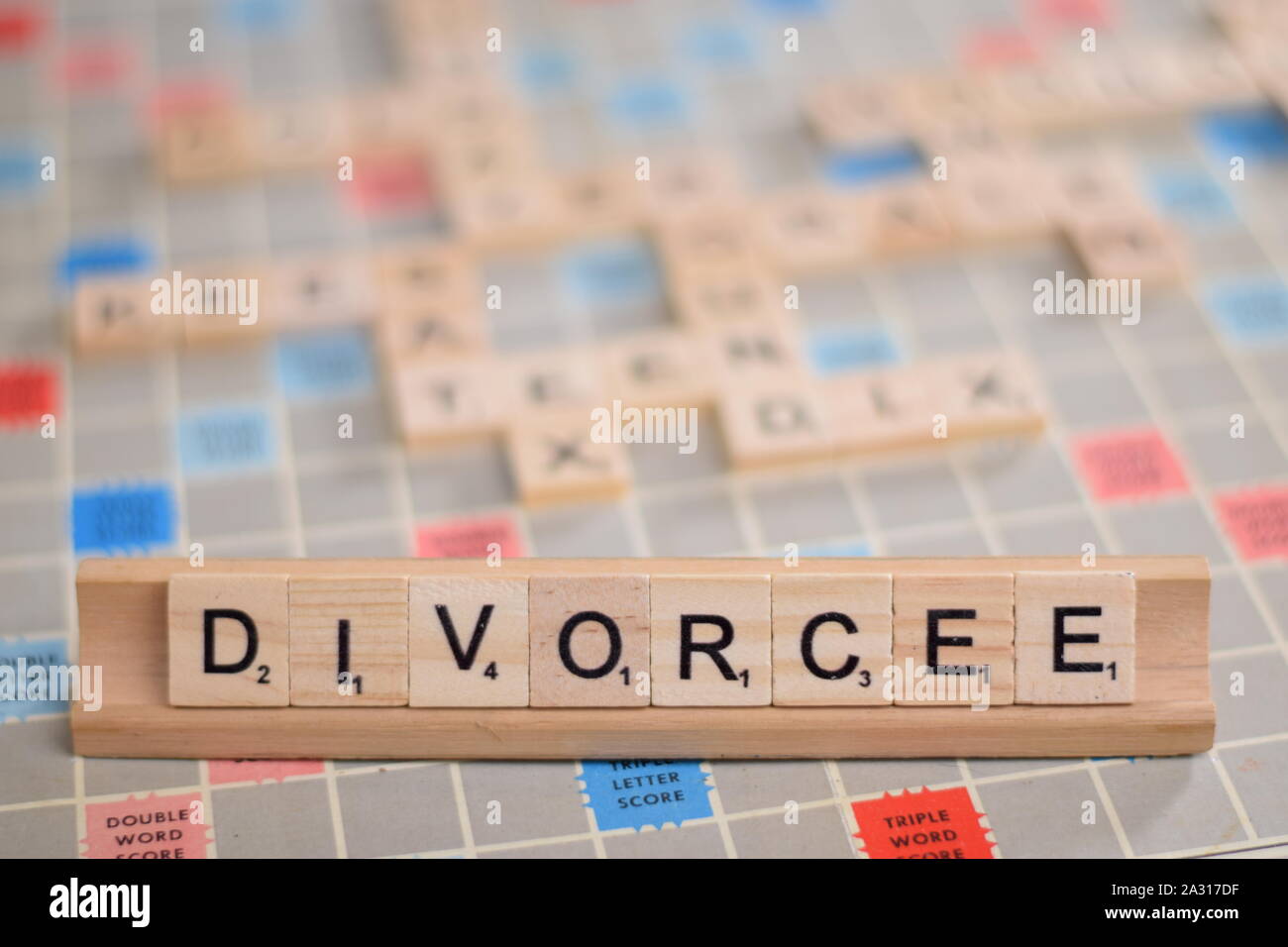 La parola francese "ivorcee" (in inglese: "ivorced') in legno piastrelle scrabble su un rack. Sullo sfondo di una scheda vintage, fuori fuoco con spazio di copia Foto Stock