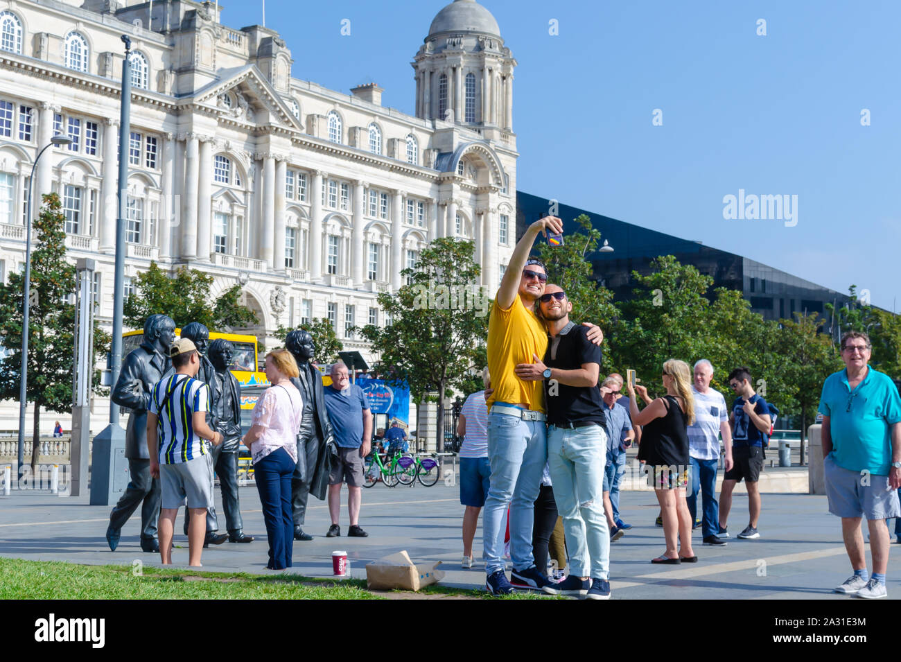 Statue in bronzo dei quattro Beatles in Liverpool, UK e una coppia gay che stanno prendendo i selfie con loro. Mostra la diversità tra i fan di banda. Foto Stock