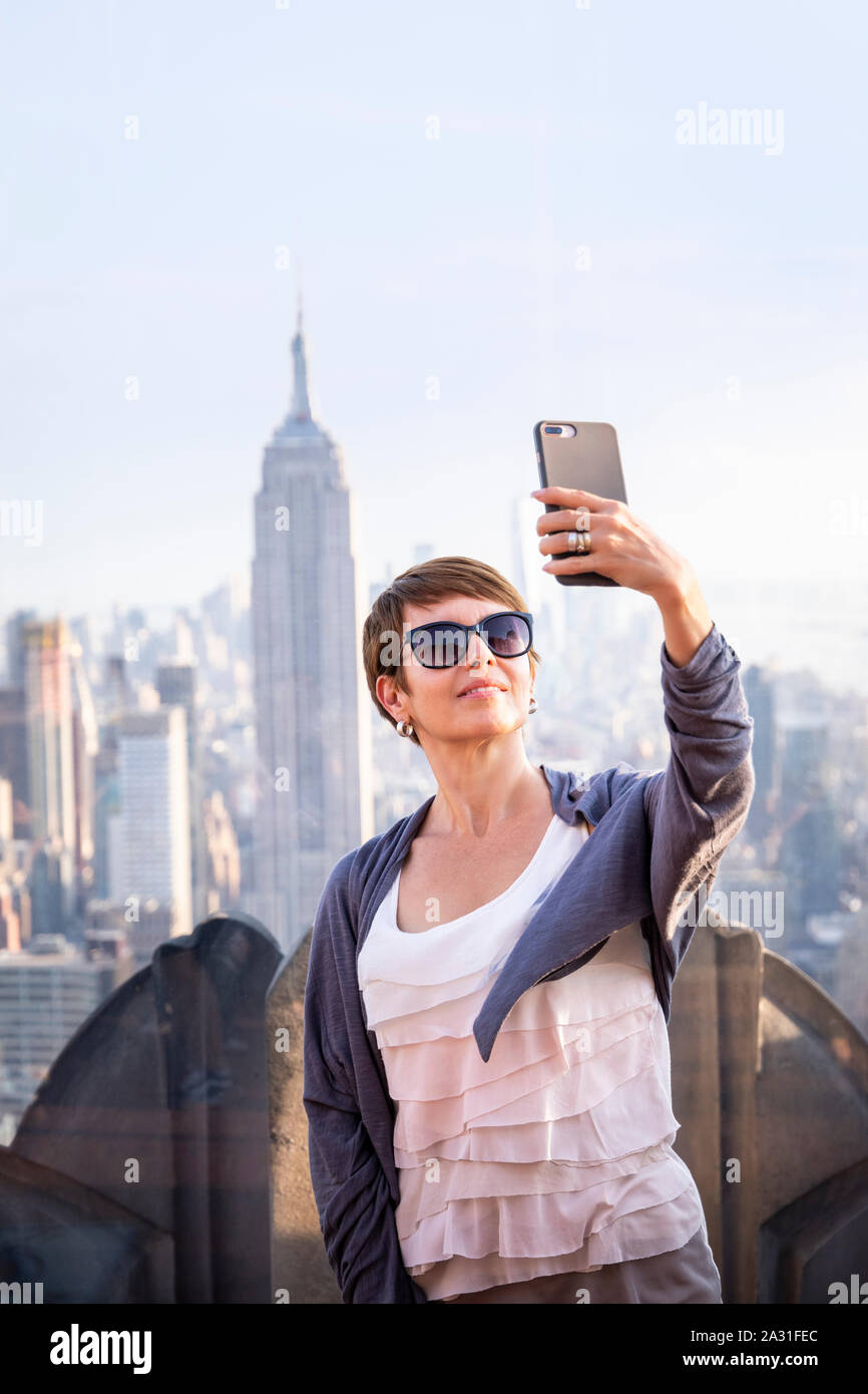 Turista femminile assume un selfie sulla sommità della roccia osservatorio con l'Empire State Building in distanza, New York City, Stati Uniti d'America. Foto Stock