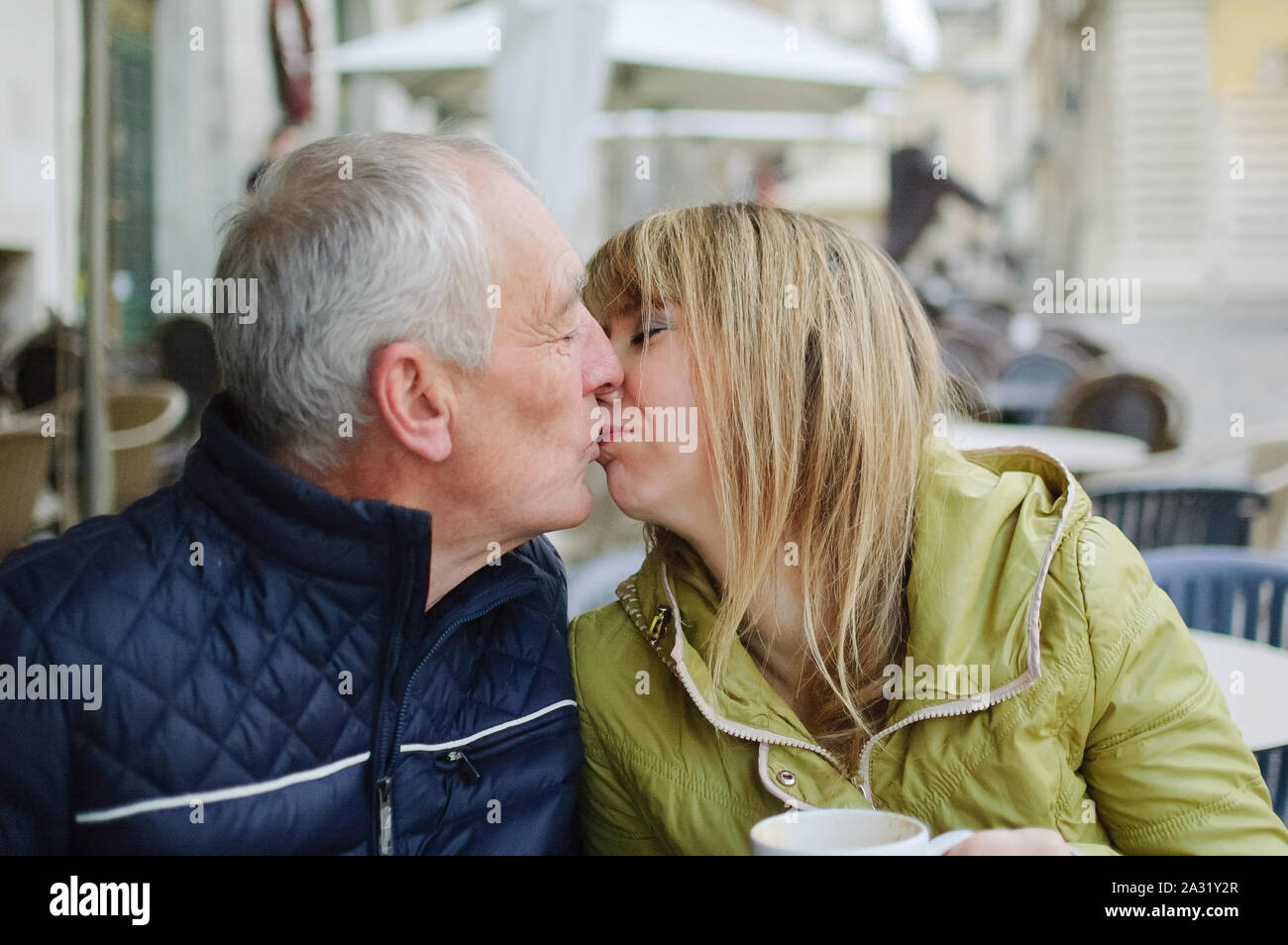 Bel uomo anziano è abbracciando la sua giovane moglie bionda di trascorrere del tempo insieme all'aperto nella città antica in primavera o in autunno. Foto Stock