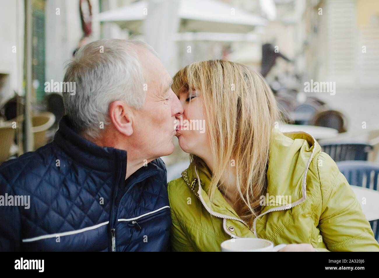 Ritratto di felice coppia romantica con differenza di età kissing all'aperto nella città antica in primavera o in autunno Foto Stock