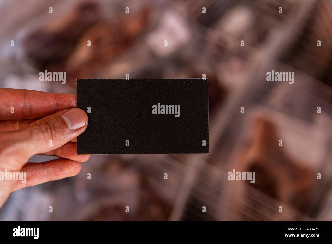 Una prospettiva in prima persona di un commerciante di mercato tenendo un piccolo business card da prodotti alimentari confezionati con copia spazio professionale per i dettagli di contatto. Foto Stock