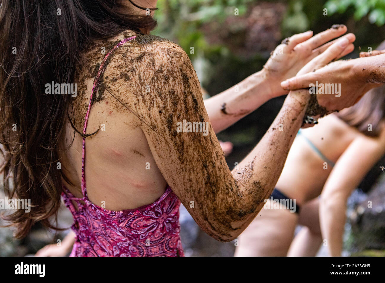 Una vista ravvicinata sulla coperta di fango del braccio di una donna in costume da bagno come essa sperimenta un tradizionale bagno di fango durante un ritiro per celebrare culture indigene. Foto Stock