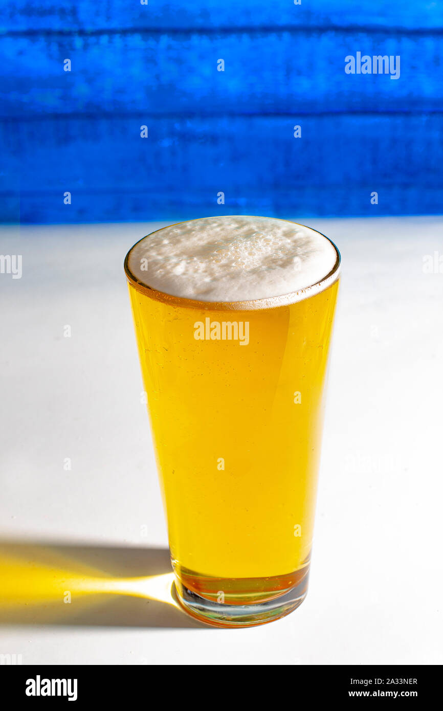 Luce pinta di birra su di un tavolo bianco con una parete in legno. Foto Stock