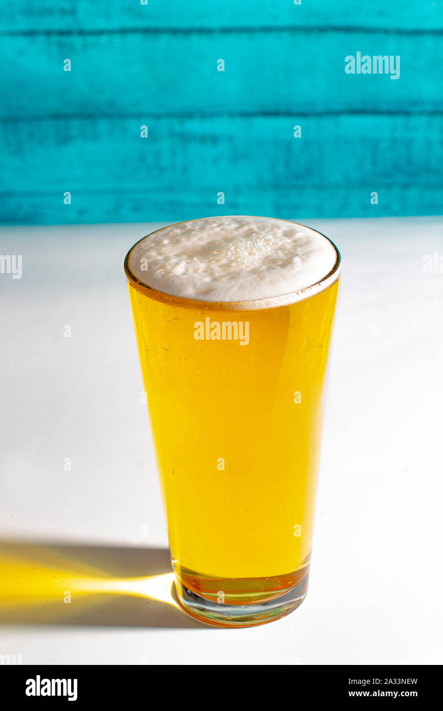 Luce pinta di birra su di un tavolo bianco con una verde parete in legno. Foto Stock