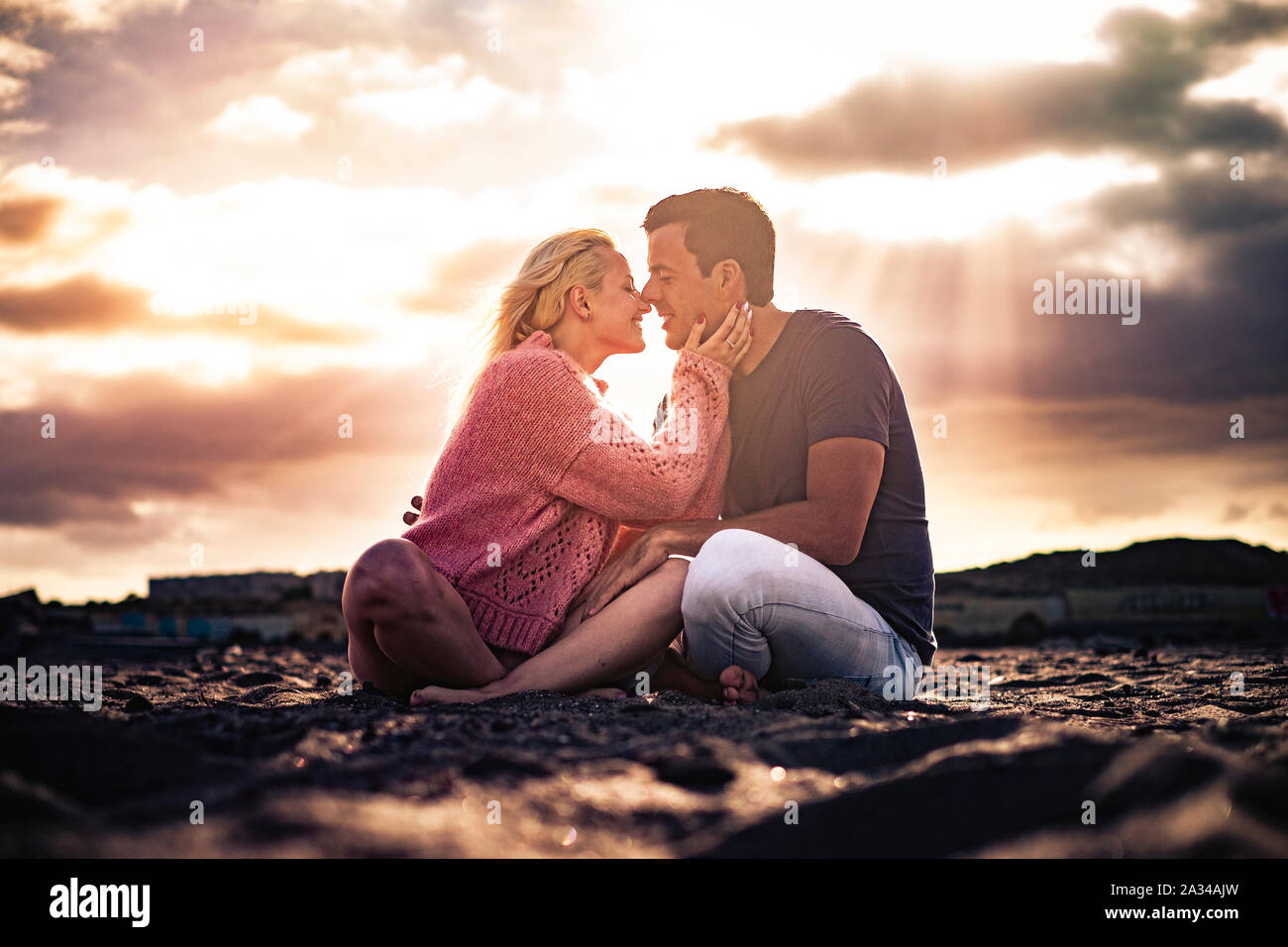 Romantico momento scenico e il concetto di amore con la giovane coppia di bella gente abbracciando e baciando sedersi sul terreno con la golden un tramonto meraviglioso in Foto Stock