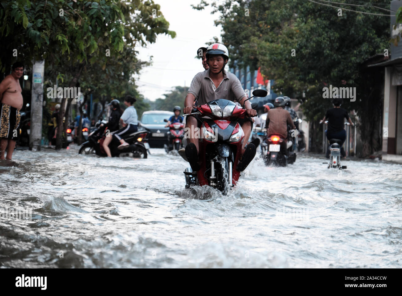 HO CHI MINH CITY, VIET NAM- Settembre 30, 2019: uomo vietnamita giro in moto con una gamba fino a croce su strada allagata con livello di acqua alta dalla marea a capodanno Foto Stock