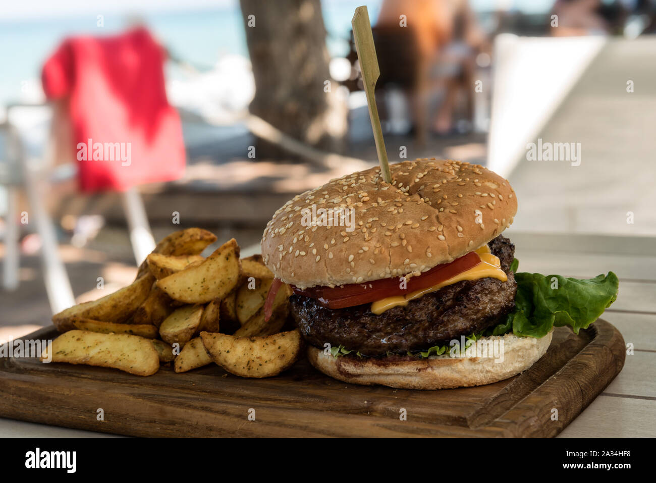 Hamburger alla griglia su tavola di legno con insalata e patatine fritte con una spiaggia in background al di fuori della messa a fuoco Foto Stock