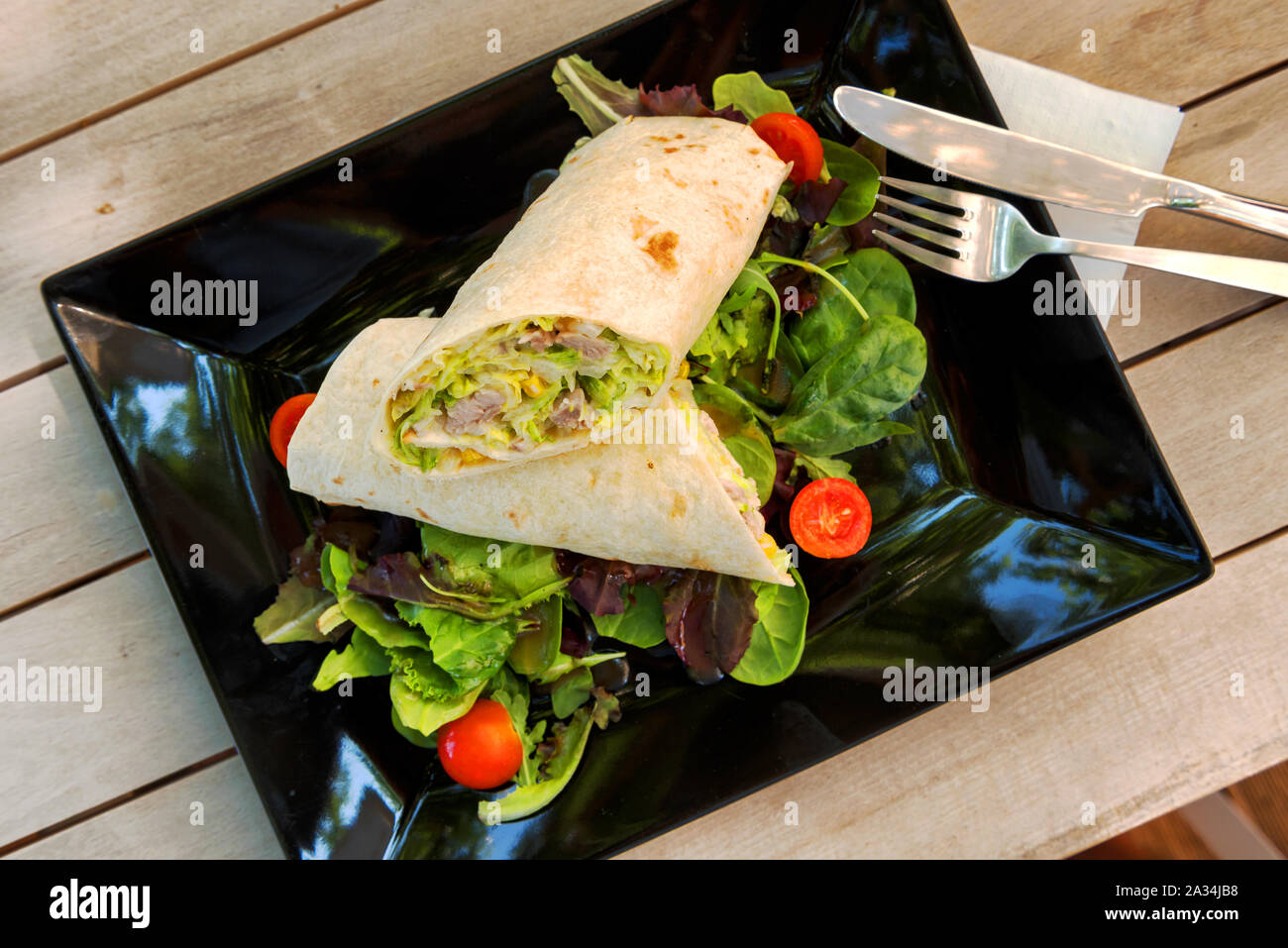 Burrito di pollo con ravanelli, peperoni, pomodori e insalata in una piastra su un tavolo di legno Foto Stock