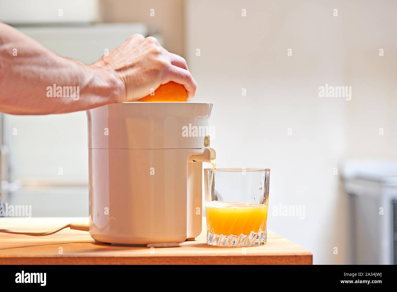Pressatura a mano la frutta di arancia con spremiagrumi elettrico in una moderna cucina Foto Stock