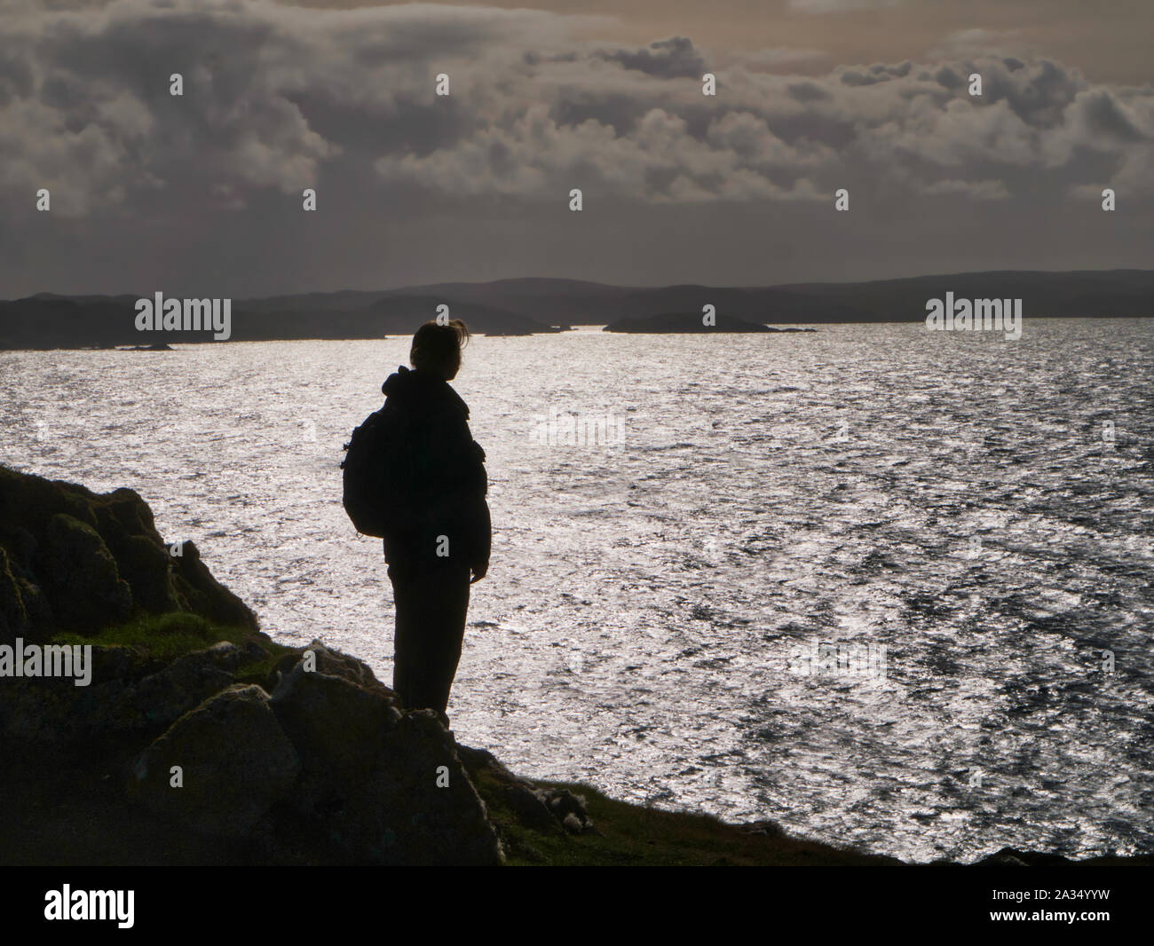 Un solitario, unica donna walker, stagliano contro il riflesso del sole sul mare - presa sulle scogliere a Sindrome di Muckle Roe nelle isole Shetland, Regno Unito Foto Stock