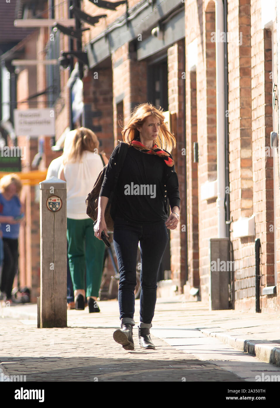 Un attraente dai capelli rossi donna che indossa di colore scuro Pantaloni e top, pizzo nero stivali e sciarpa colorata. Di età tardo 30s. Back lit. Foto Stock Un attraente dai capelli rossi donna che indossa di colore scuro Pantaloni e top, pizzo nero stivali e sciarpa colorata. Di età tardo 30s. Back lit. Foto Stock