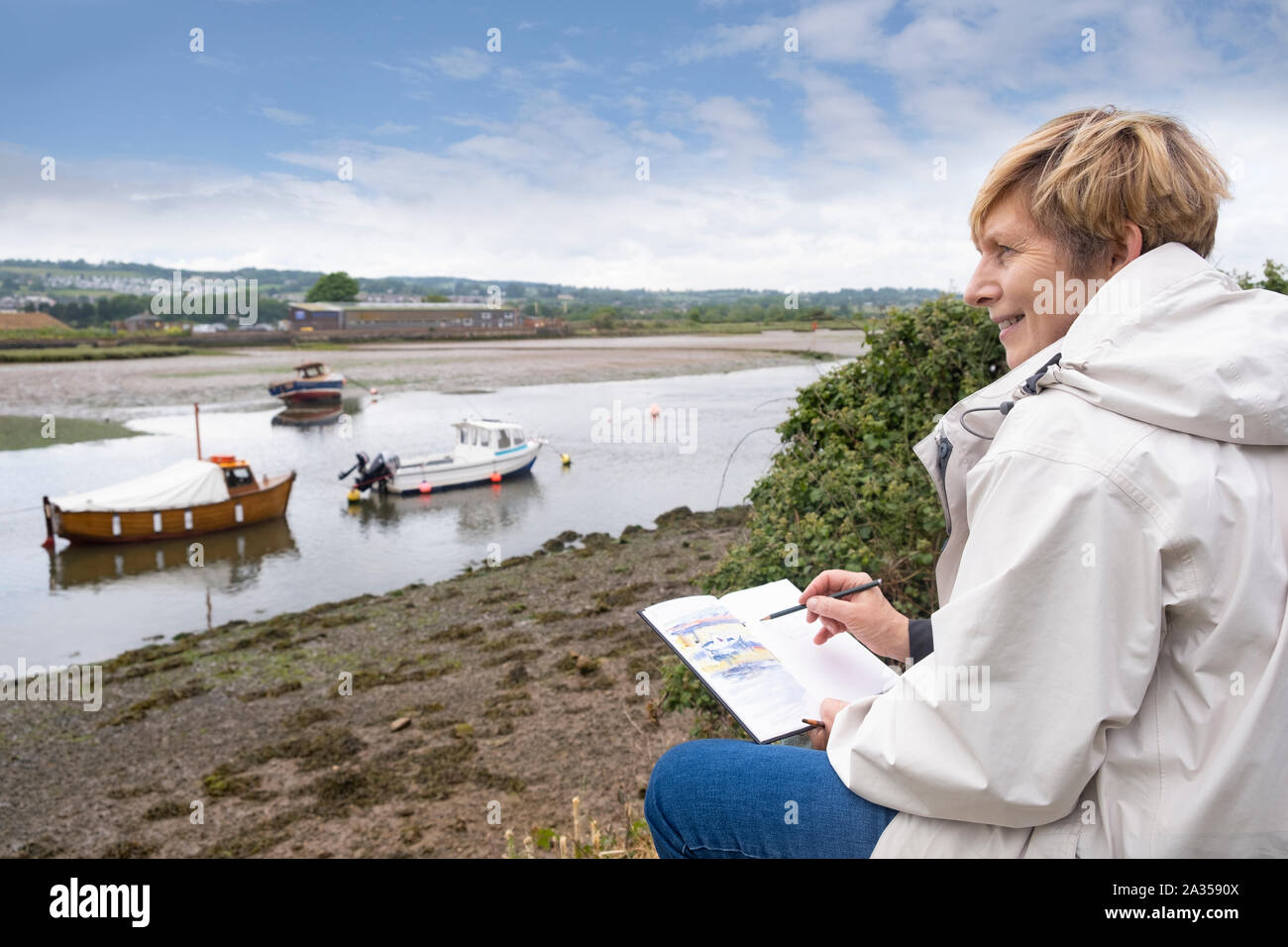 Senior donna godendo il pensionamento disegno esterno vicino Regno Unito estuario del fiume in vacanza, casual da indossare abiti caldi Foto Stock