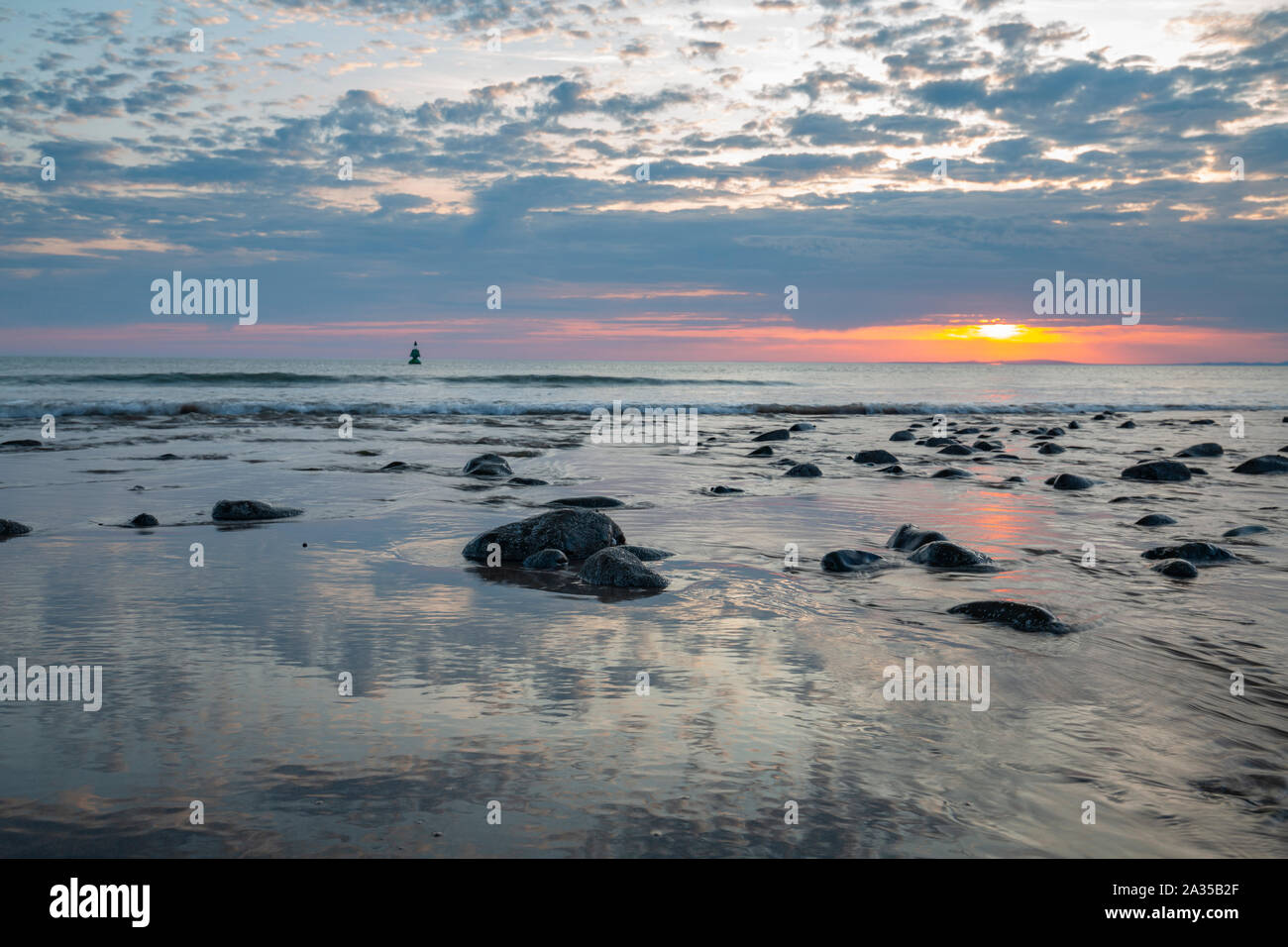 Le onde del mare il lavaggio costa rocciosa riflettendo colorato tramonto Cielo in Caernarfon, Regno Unito Foto Stock