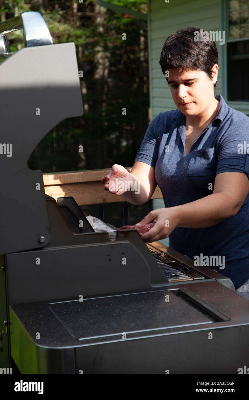 Donna mette un pezzo di hamburger sul barbeque in una serata estiva Foto Stock