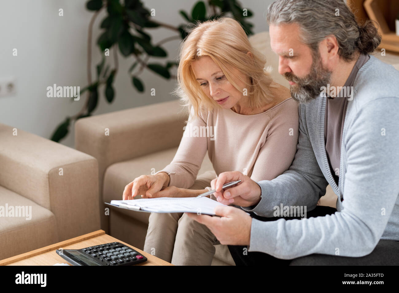 Barbuto uomo maturo puntando al contratto durante la lettura con sua moglie Foto Stock