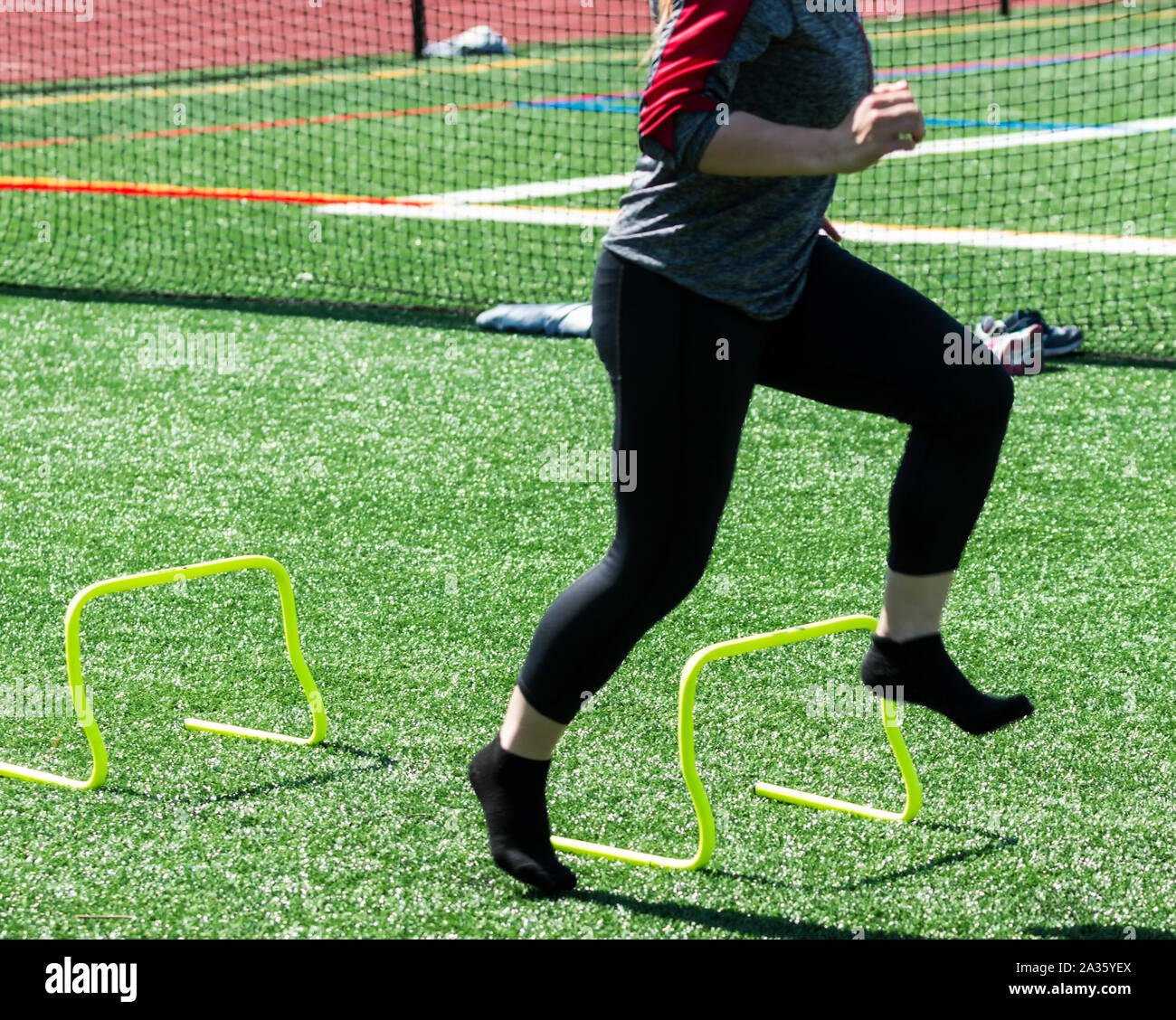 Una femmina di alta scuola atleta è in esecuzione senza scarpe su mini giallo banana ostacoli durante la velocità, la potenza e la flessibilità della formazione su un tappeto erboso verde. Foto Stock