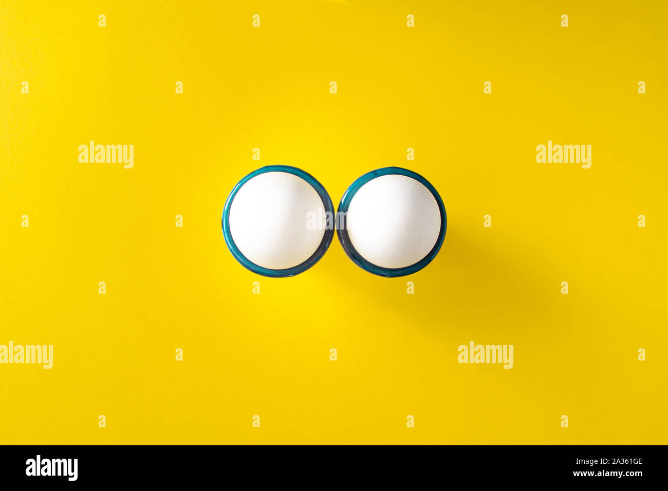 Due le uova bianche nell'uovo si erge su sfondo giallo. Mondo uovo concetto giorno Foto Stock