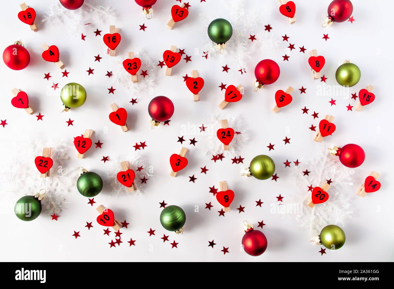 Avvento calandra numeri sul cuore rosso da neve decorativa e palle di Natale di colori rosso e verde. Concetto di Natale lay piatto Foto Stock