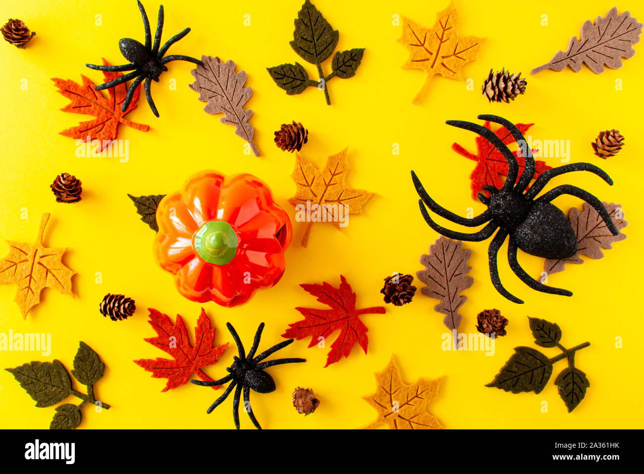 Vista di zucca, foglie di autunno, nero ragni e pigne su sfondo giallo. Concetto di Halloween, laici piatta Foto Stock