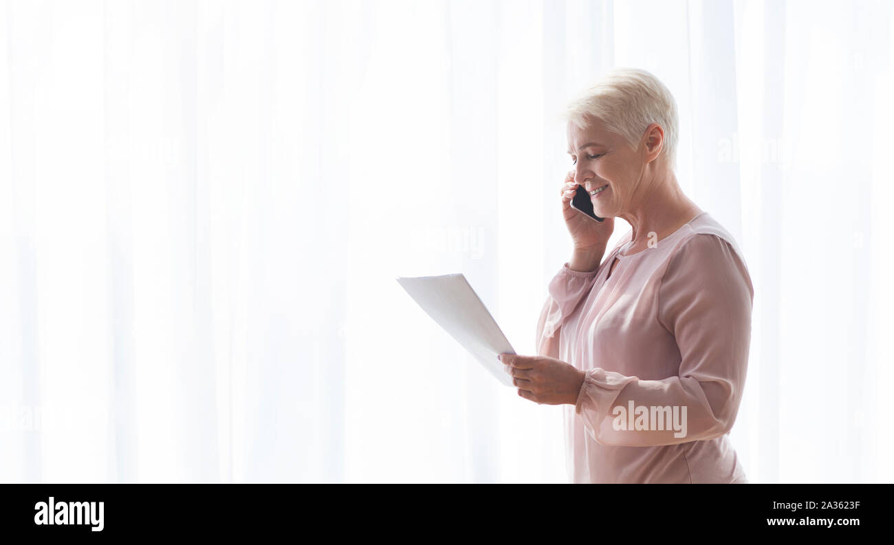 Età della donna azienda documenti e parla al telefono con i clienti Foto Stock