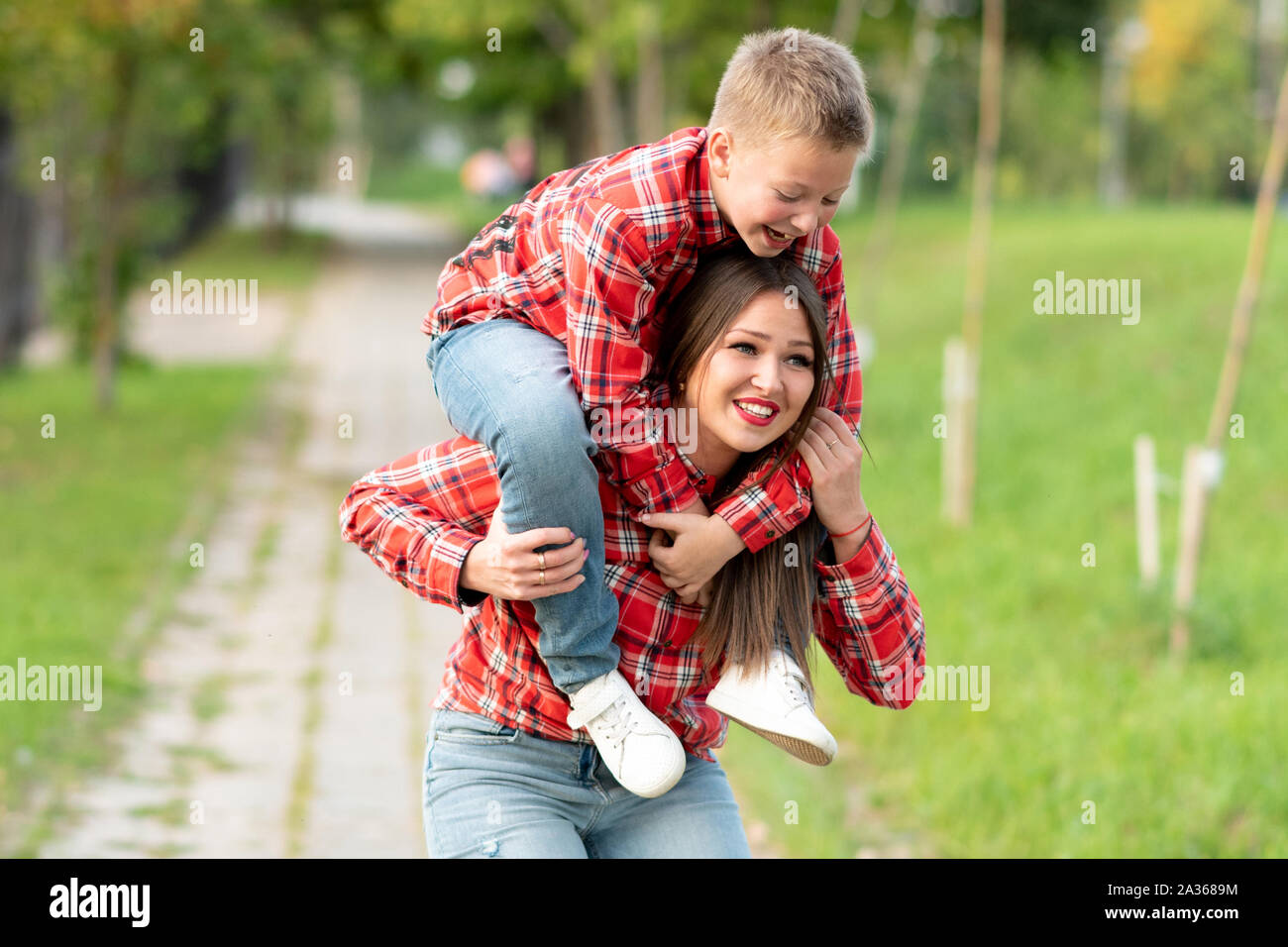Mom con uno stupito espressione sul viso, piegati, detiene un sorridente figlio sulle sue spalle. Foto Stock