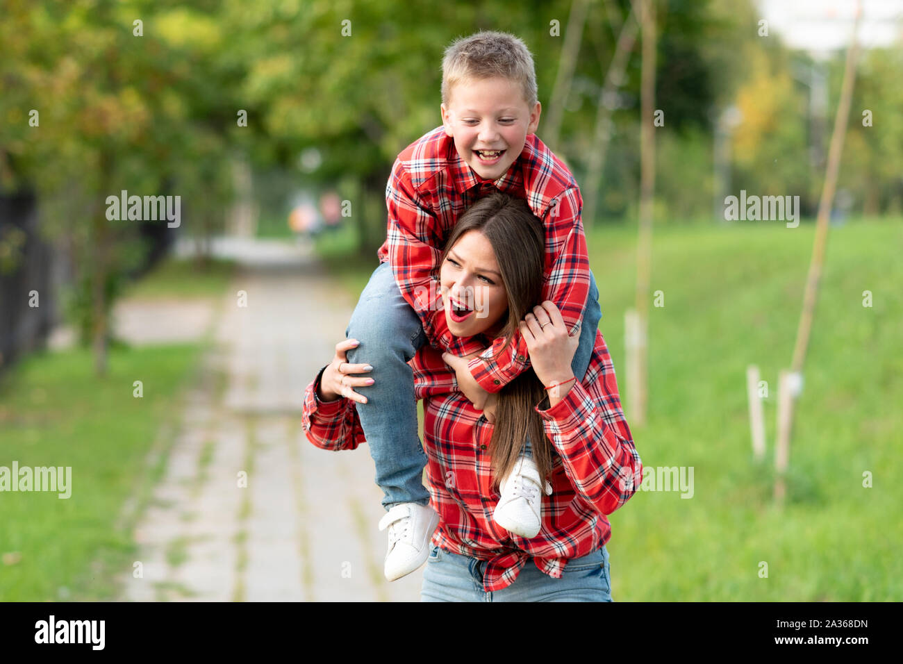 Mom con uno stupito espressione sul viso, detiene un sorridente figlio sulle sue spalle. Foto Stock