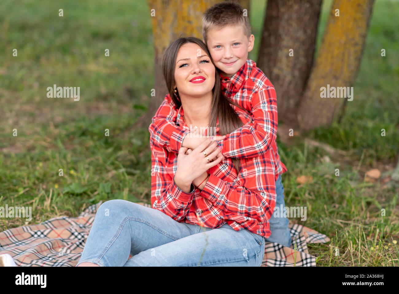Il figlio dolcemente abbracci di sua madre alle spalle, entrambi sorridenti, seduto su un copriletto a scacchi. Foto Stock