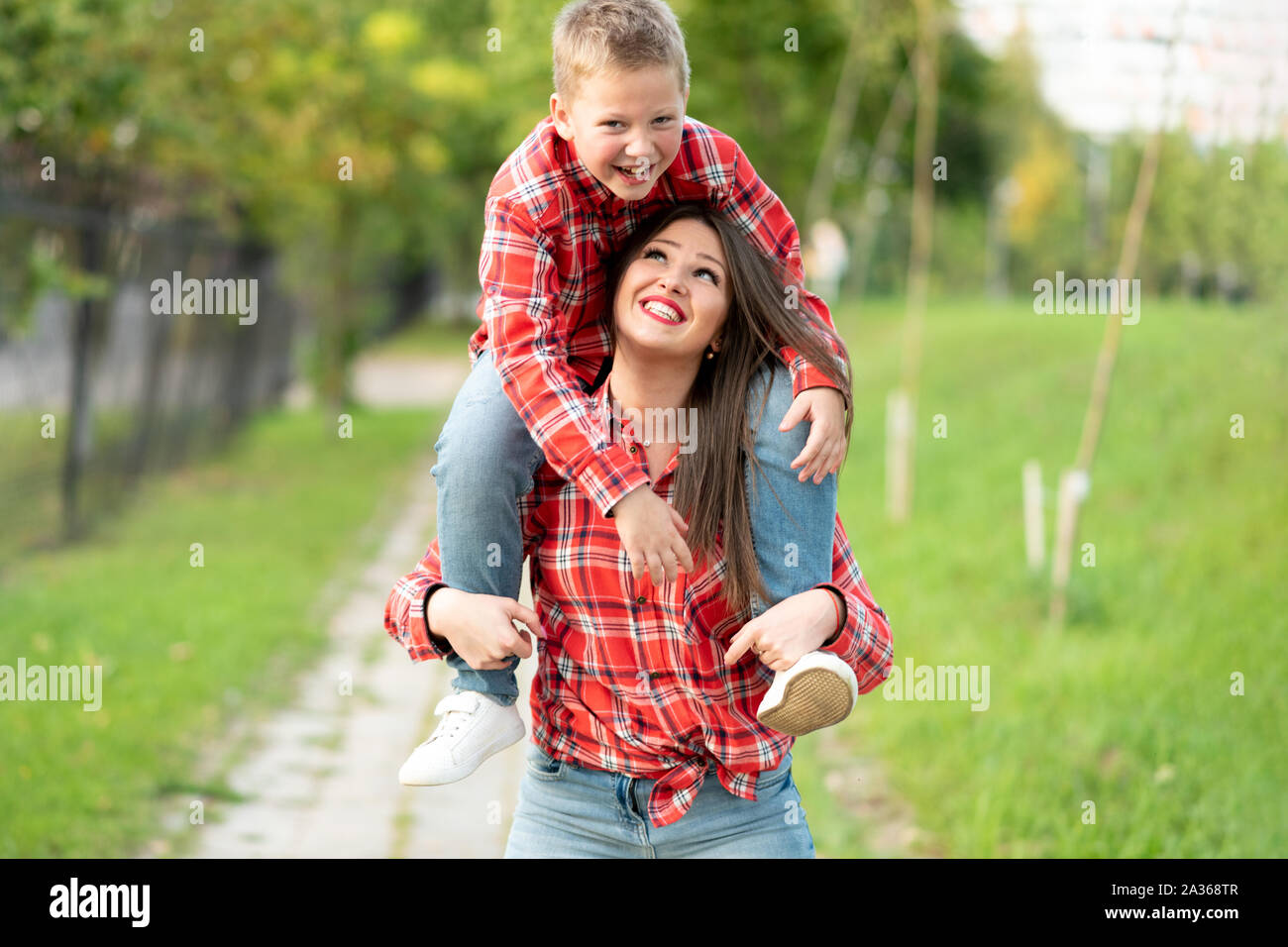 Mom, sorridente, porta un ridere figlio sulle sue spalle. Foto Stock