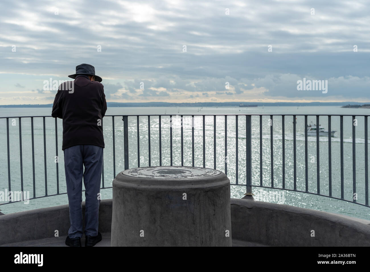 Un uomo in piedi da solo guardando oltre le ringhiere in mare contemplando Foto Stock