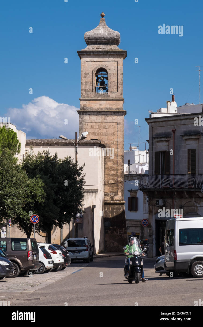 Uno scooter per le strade con un campanile sullo sfondo come visibile da Via Armando Diaz, Ostuni, Italia Foto Stock
