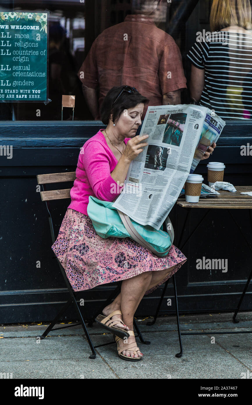 Una donna di mezza età trascorre la domenica mattina dalla lettura di un quotidiano e un caffè al bar esterno tavolo. Seattle, Washington, Stati Uniti d'America. Foto Stock