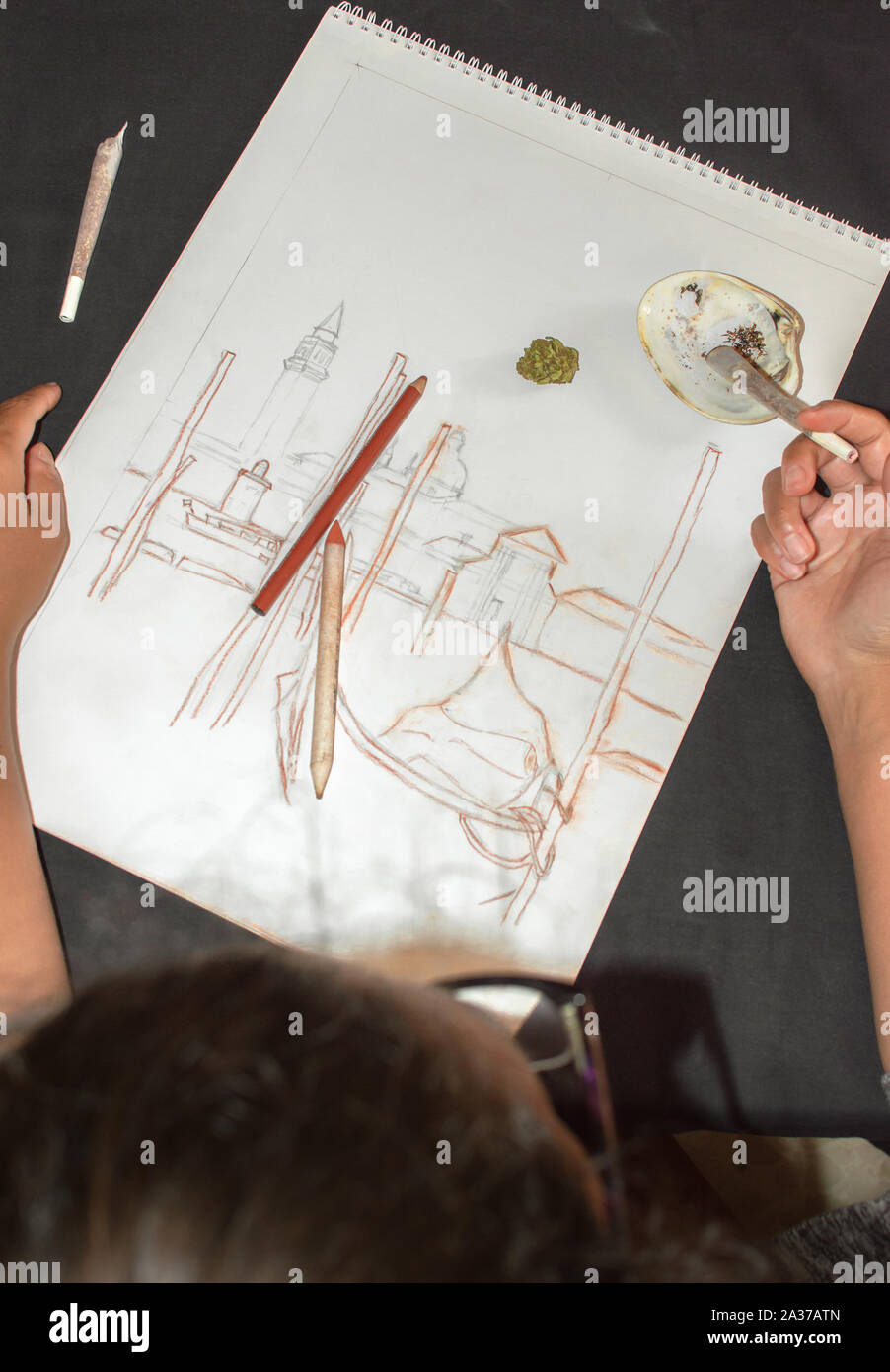 La donna a fumare marijuana giunto durante una pausa dopo il disegno. Sfondo con la cannabis bud, schizzo e shell posacenere. Concetto di droga nell'arte. Foto Stock