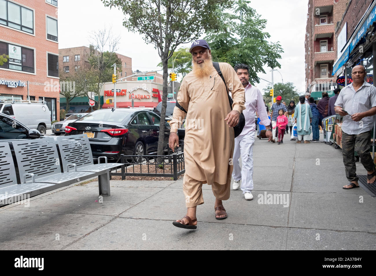 Un uomo musulmano in un cappuccio Yankee e abito tradizionale passeggiate sulla 37th Avenue a Jackson Heights, Queens, a New York City. Foto Stock
